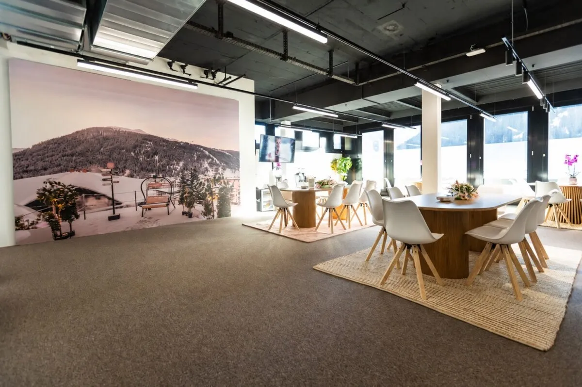 Round wooden tables with white chairs beside large windows onto snowy slopes