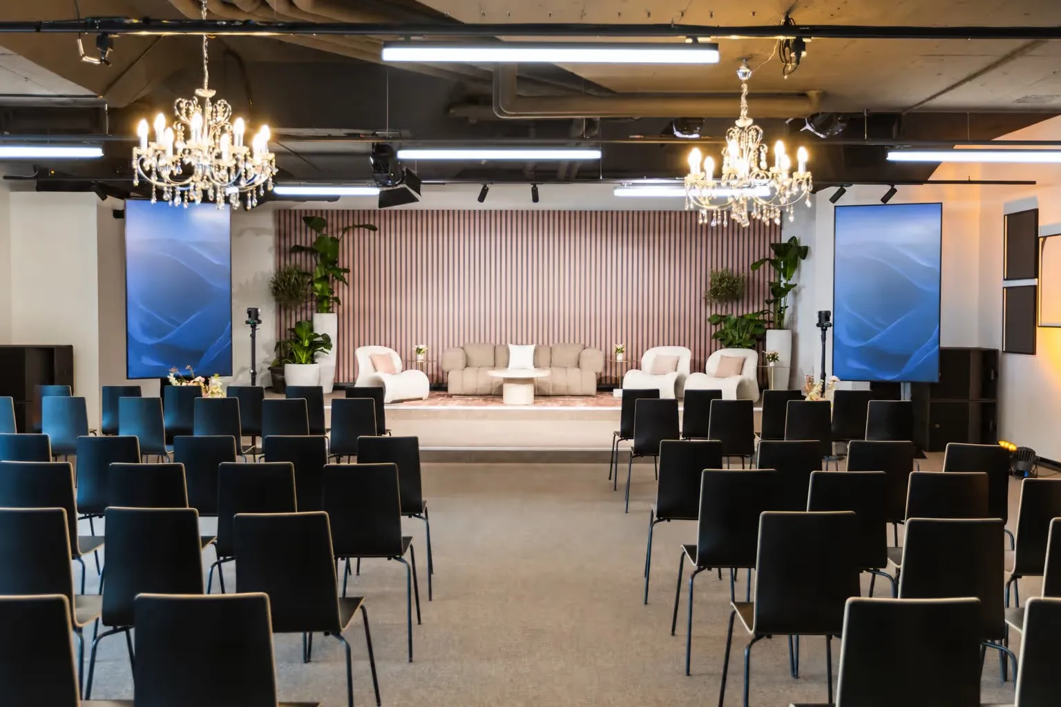 The stage of the Davos Event Lounge with lounge seating, two chandeliers and rows of chairs
